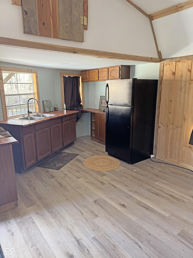 kitchen featuring light wood finished floors, vaulted ceiling, freestanding refrigerator, and a sink