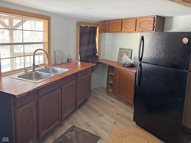 kitchen featuring light wood-style flooring, butcher block countertops, freestanding refrigerator, and a sink