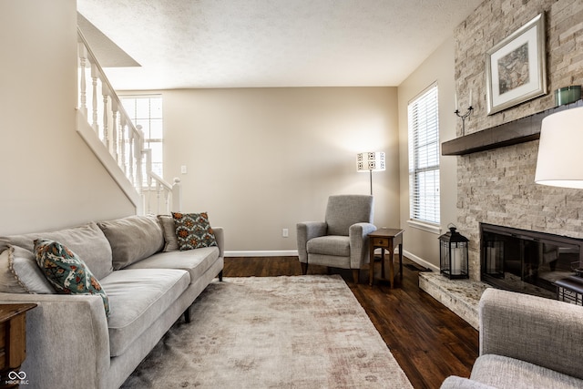 living area with a stone fireplace, dark wood-type flooring, baseboards, and a textured ceiling