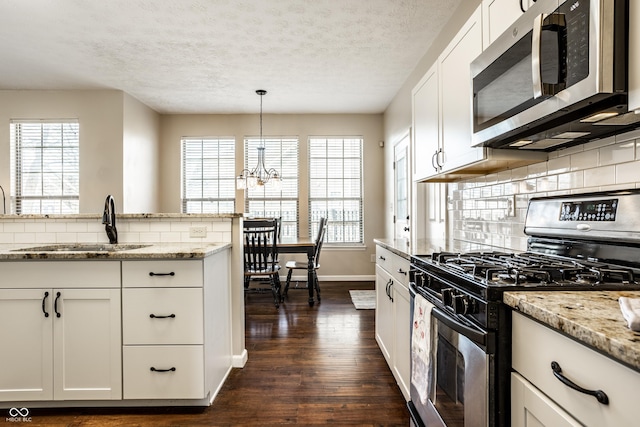 kitchen featuring light stone countertops, dark wood finished floors, a sink, appliances with stainless steel finishes, and backsplash