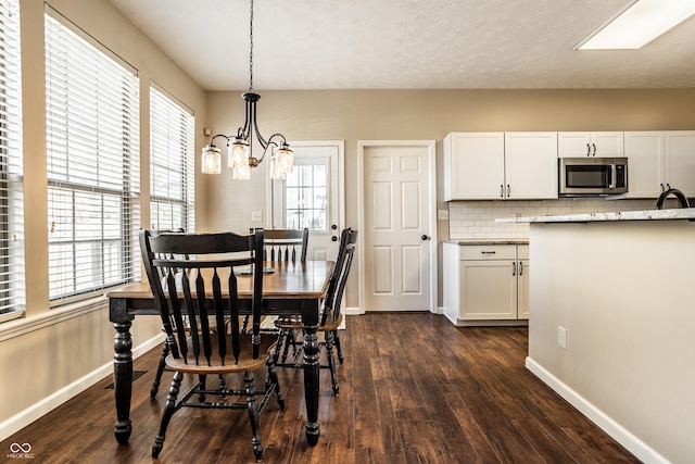 dining room with dark wood-type flooring, a notable chandelier, and baseboards