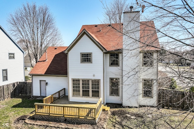 back of property with a chimney, a wooden deck, a fenced backyard, and a shingled roof