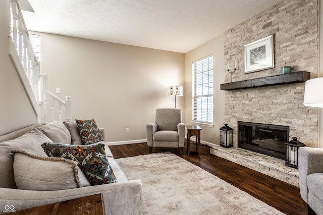 living room with dark wood-type flooring, baseboards, stairway, a stone fireplace, and a textured ceiling