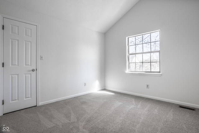 carpeted spare room featuring visible vents, baseboards, and vaulted ceiling