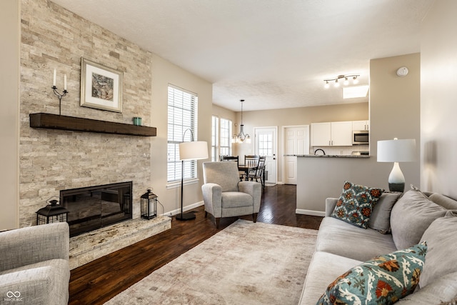 living room with baseboards, a textured ceiling, a stone fireplace, and dark wood-style floors