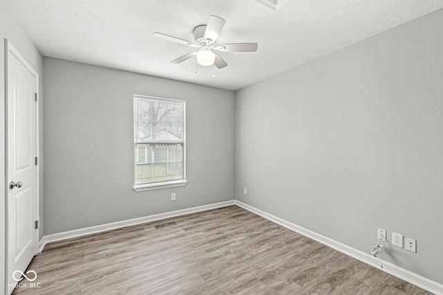 empty room with a ceiling fan, visible vents, wood finished floors, baseboards, and a textured ceiling