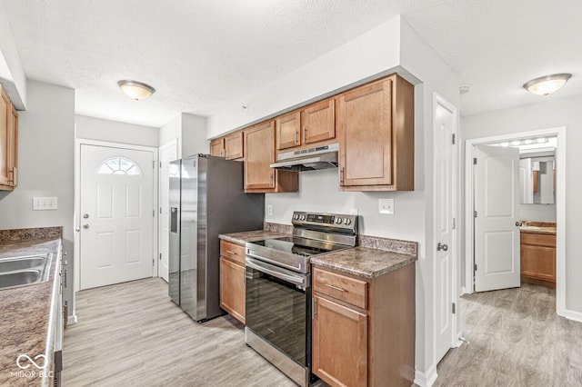 kitchen with under cabinet range hood, light wood-style flooring, stainless steel appliances, brown cabinetry, and a textured ceiling