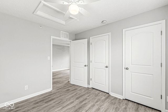 unfurnished bedroom featuring visible vents, a ceiling fan, light wood-style floors, baseboards, and attic access