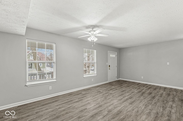 spare room featuring baseboards, dark wood-type flooring, a ceiling fan, and a textured ceiling