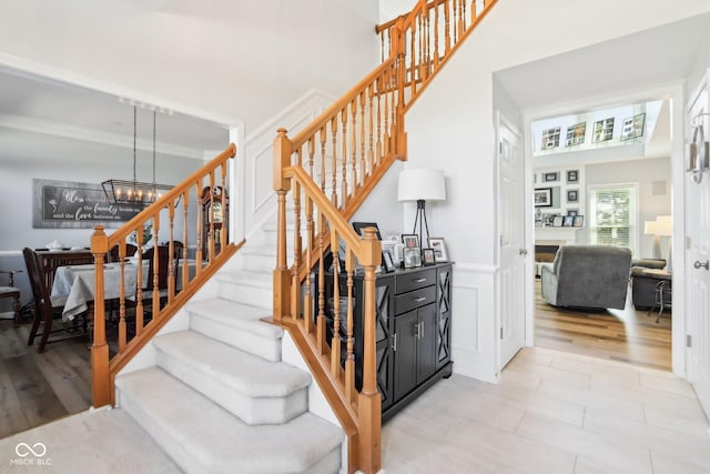 stairs featuring a wainscoted wall, wood finished floors, crown molding, a decorative wall, and a chandelier