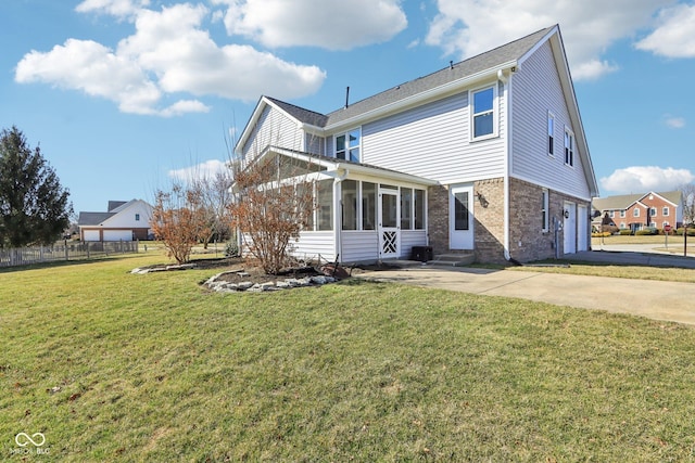 rear view of house featuring a yard, a sunroom, concrete driveway, a garage, and brick siding