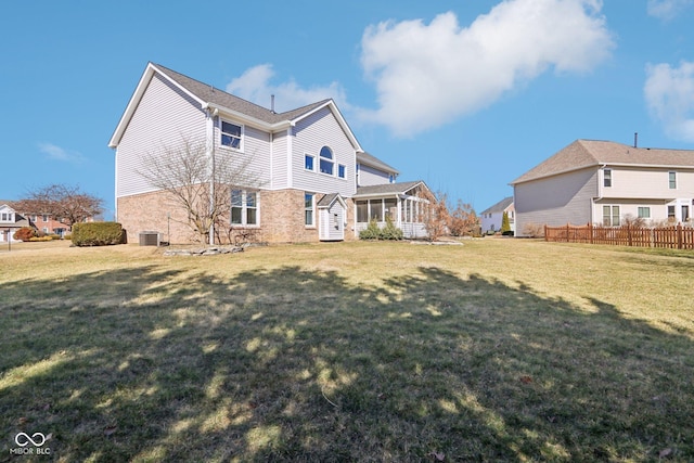 rear view of house featuring central AC, fence, a yard, a sunroom, and brick siding