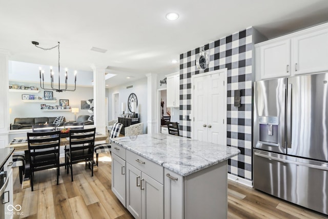 kitchen with a kitchen island, stainless steel fridge with ice dispenser, open floor plan, light wood-style flooring, and ornate columns