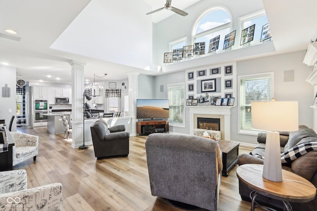 living room featuring light wood finished floors, decorative columns, ceiling fan with notable chandelier, recessed lighting, and a glass covered fireplace