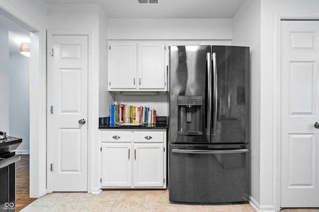 kitchen with dark countertops, visible vents, baseboards, fridge with ice dispenser, and white cabinets