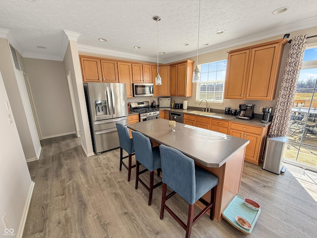 kitchen with a breakfast bar area, a kitchen island, light wood-style flooring, a sink, and appliances with stainless steel finishes