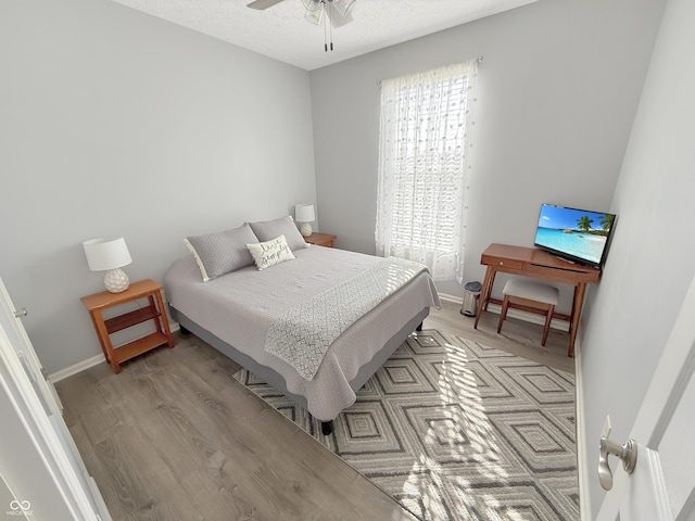 bedroom featuring light wood-type flooring, baseboards, a textured ceiling, and ceiling fan