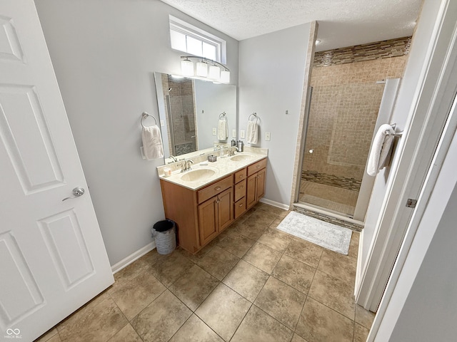 bathroom with baseboards, double vanity, a stall shower, a sink, and a textured ceiling