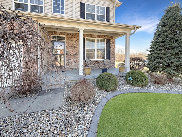 entrance to property featuring brick siding, covered porch, and a yard