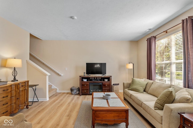 living room with light wood-style flooring, a textured ceiling, stairs, and baseboards