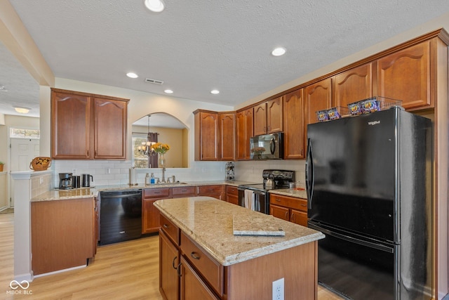 kitchen with light wood-type flooring, black appliances, tasteful backsplash, a center island, and light stone countertops