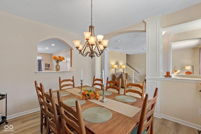 dining room featuring light wood-type flooring, baseboards, stairs, and ornate columns