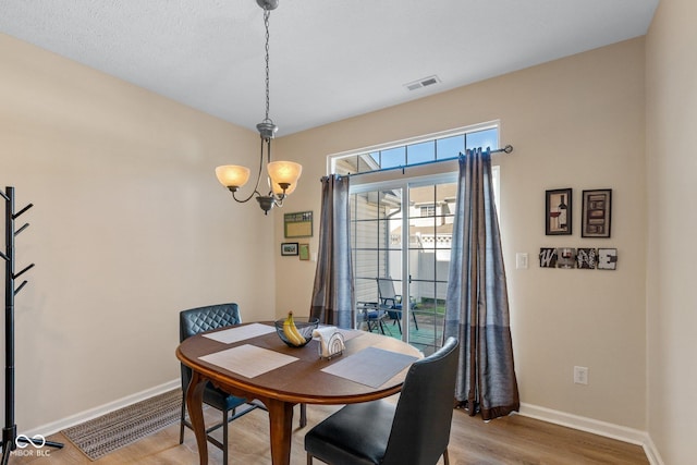 dining area with visible vents, baseboards, light wood-type flooring, and a chandelier