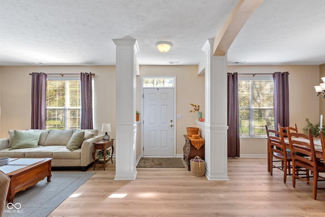 foyer with light wood finished floors, plenty of natural light, a textured ceiling, and ornate columns