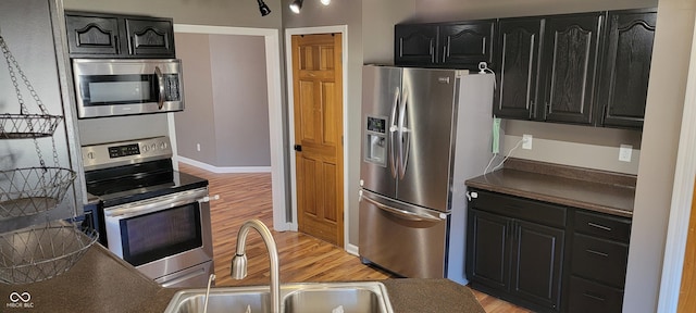 kitchen featuring a sink, dark countertops, dark cabinetry, stainless steel appliances, and light wood finished floors