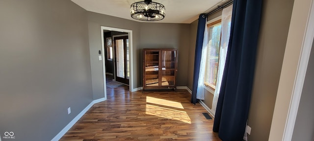 hallway featuring a chandelier, baseboards, visible vents, and wood finished floors