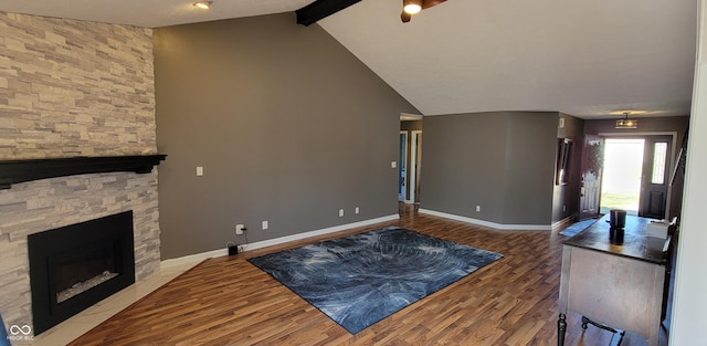 living room with wood finished floors, baseboards, a ceiling fan, lofted ceiling with beams, and a stone fireplace