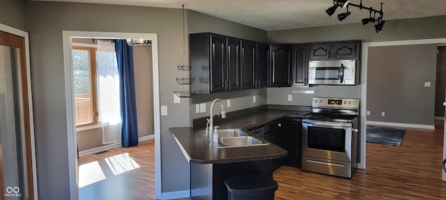 kitchen featuring dark wood finished floors, a sink, appliances with stainless steel finishes, a textured ceiling, and dark countertops