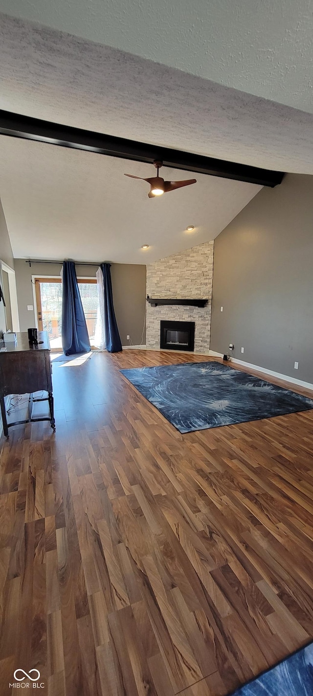 unfurnished living room featuring a stone fireplace, a textured ceiling, vaulted ceiling with beams, and wood finished floors