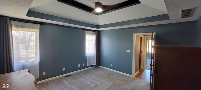 spare room with visible vents, a raised ceiling, carpet, and baseboards