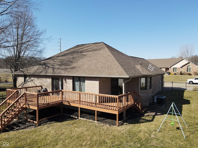 rear view of house with a lawn, a deck, central AC, fence, and roof with shingles