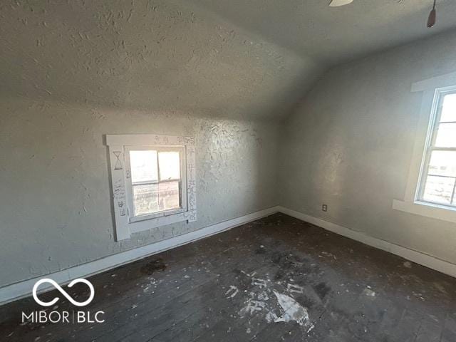 bonus room featuring baseboards, a textured ceiling, lofted ceiling, and a textured wall