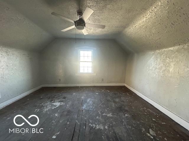 additional living space with a textured wall, wood-type flooring, a textured ceiling, and vaulted ceiling