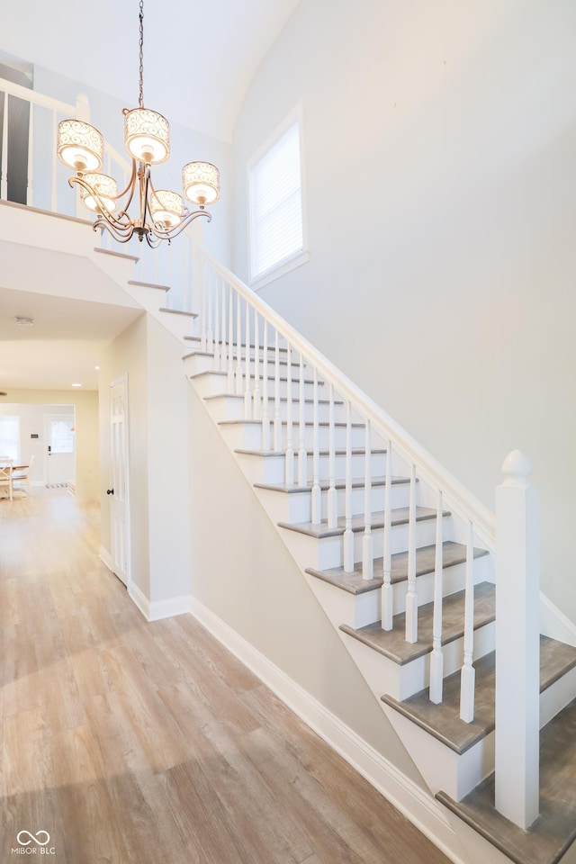 staircase featuring wood finished floors, baseboards, a towering ceiling, and a chandelier