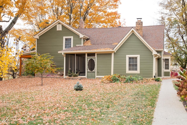 traditional-style house featuring a front yard, a shingled roof, a chimney, and a sunroom