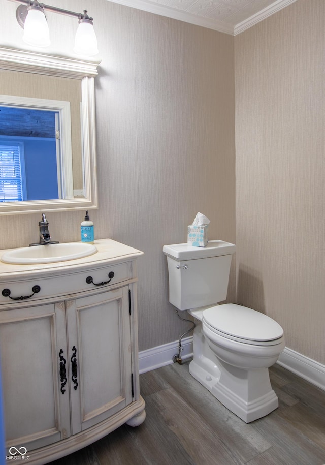 half bathroom with vanity, wood finished floors, baseboards, ornamental molding, and toilet