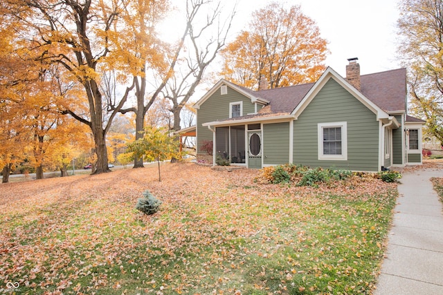 back of house featuring roof with shingles, a sunroom, and a chimney