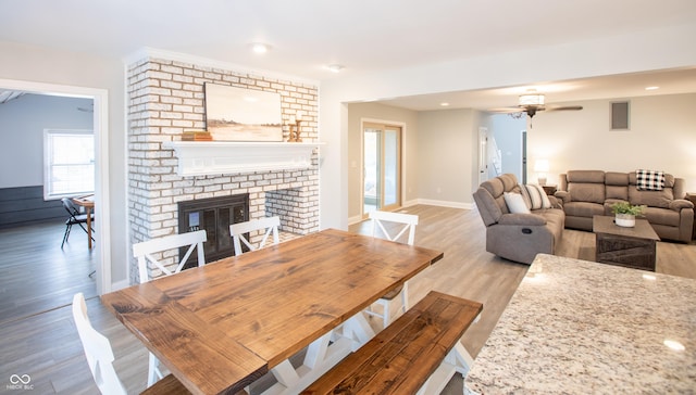 living area featuring visible vents, a ceiling fan, a fireplace, light wood finished floors, and baseboards