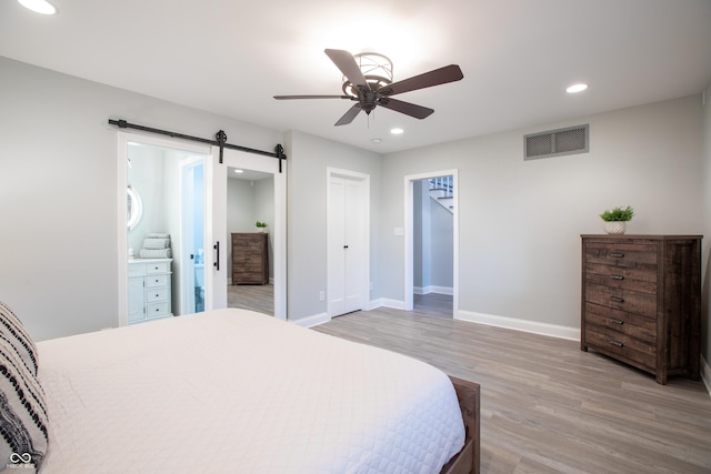 bedroom with a barn door, recessed lighting, light wood-style floors, and visible vents