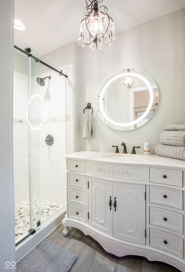 bathroom featuring wood finished floors, a notable chandelier, a stall shower, and vanity