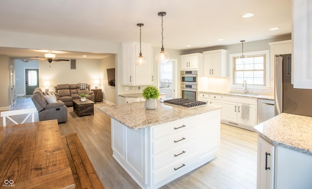 kitchen featuring a center island, light stone countertops, light wood-style flooring, stainless steel appliances, and a sink