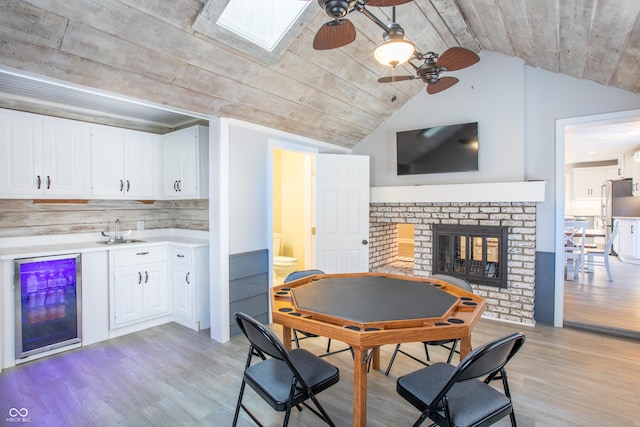 dining space featuring wine cooler, light wood-style flooring, a fireplace, and vaulted ceiling