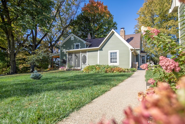 view of front of house featuring a shingled roof, a front lawn, a sunroom, and a chimney