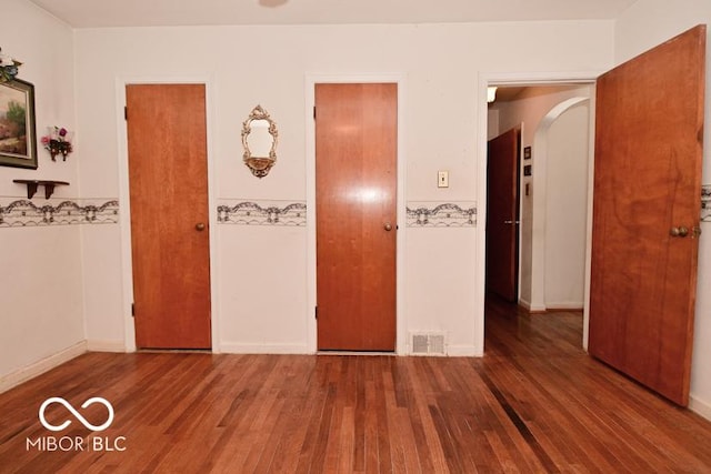 unfurnished bedroom with arched walkways, wood finished floors, visible vents, and baseboards