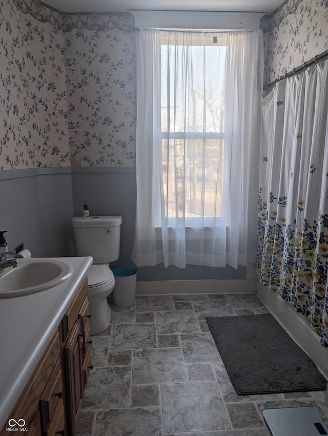 bathroom with vanity, shower / tub combo, toilet, and a healthy amount of sunlight