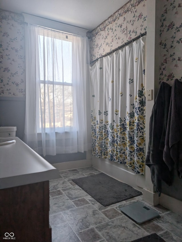 full bathroom featuring wallpapered walls, shower / tub combo with curtain, and stone finish flooring